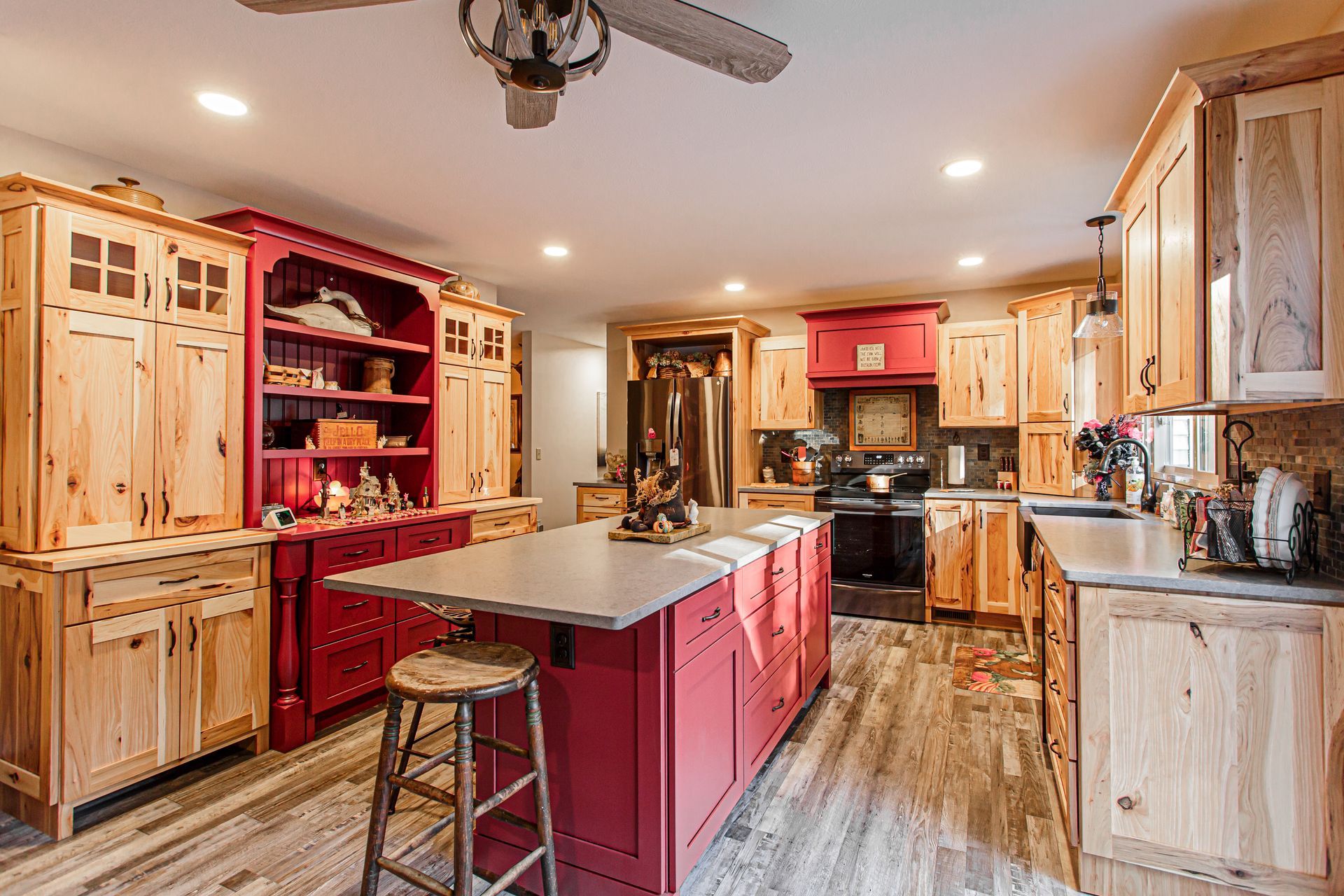 Rustic kitchen with red island and cabinets, light wood cabinets, and gray countertop.