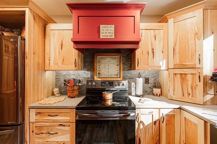 Kitchen with light wood cabinets, red range hood, black stove, and a decorative clock.