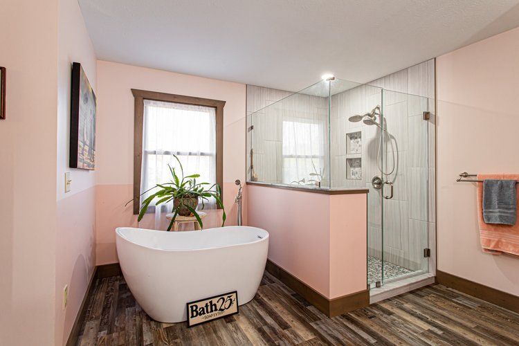 Pink bathroom with white soaking tub, glass shower, and wood-look floor.
