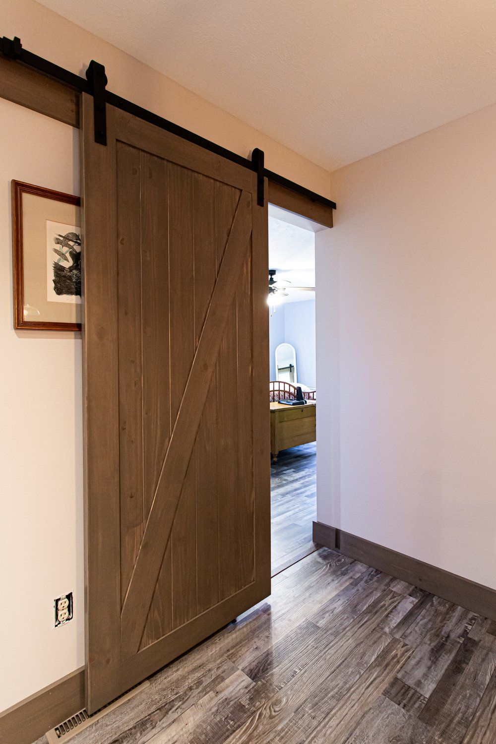 Barn door on a track, gray wood, angled design, leading into a room with furniture and light.