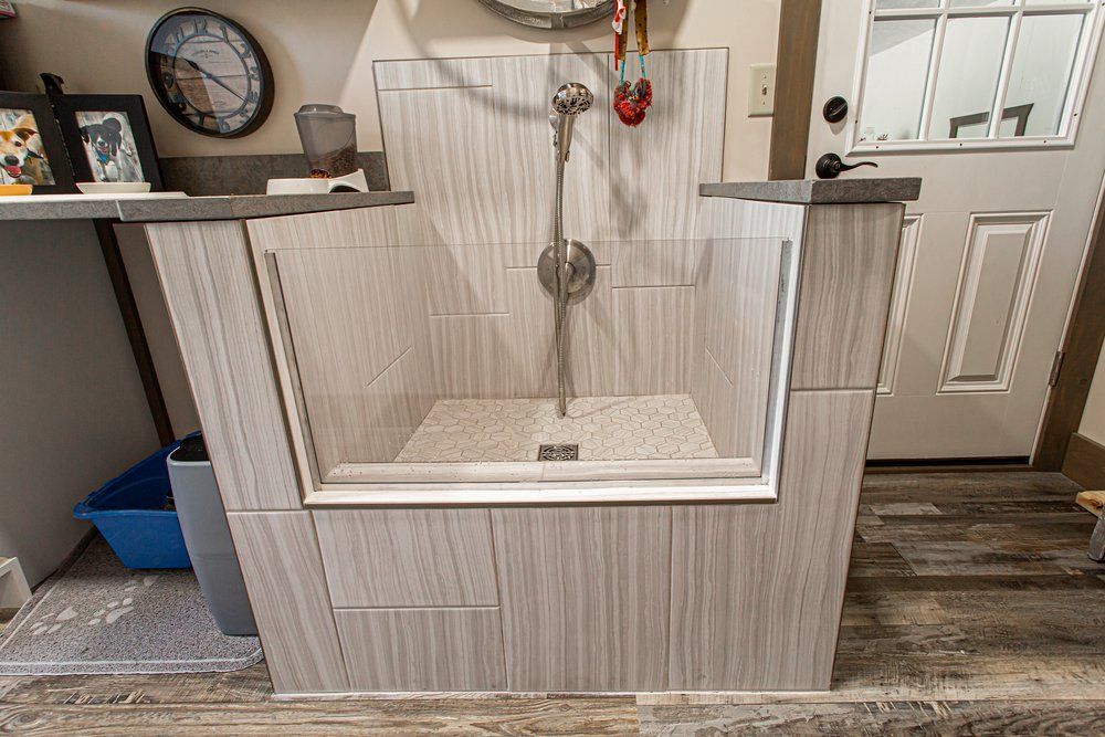 Dog washing station with tiled walls, glass doors, and shower head in a room.