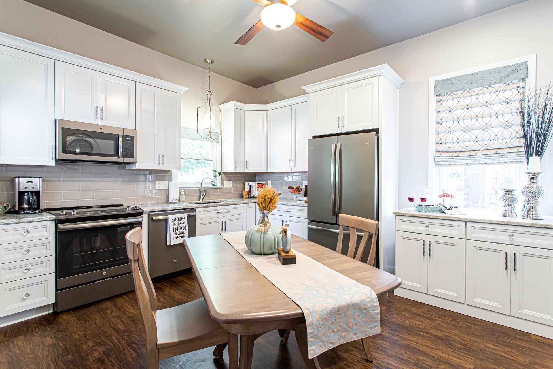 Bright white kitchen with stainless steel appliances, dark wood floors, and a dining table.