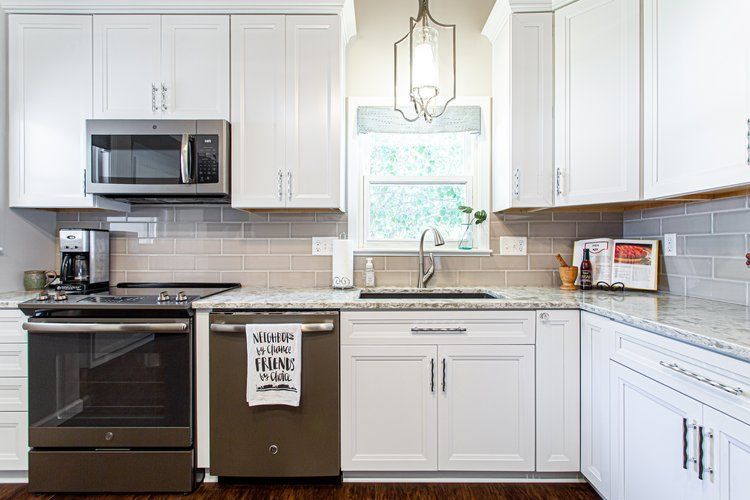 White kitchen with stainless steel appliances, light gray backsplash, and granite countertops.
