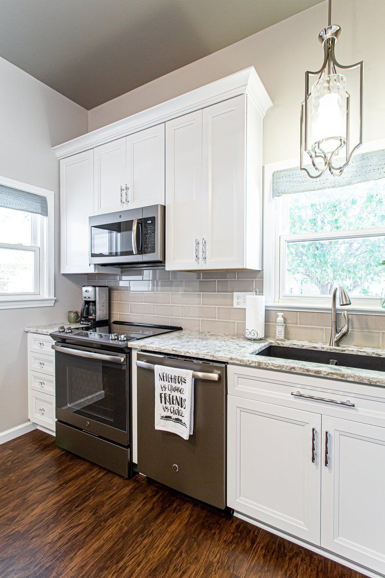White kitchen with stainless steel appliances, countertops, and dark wood floors.