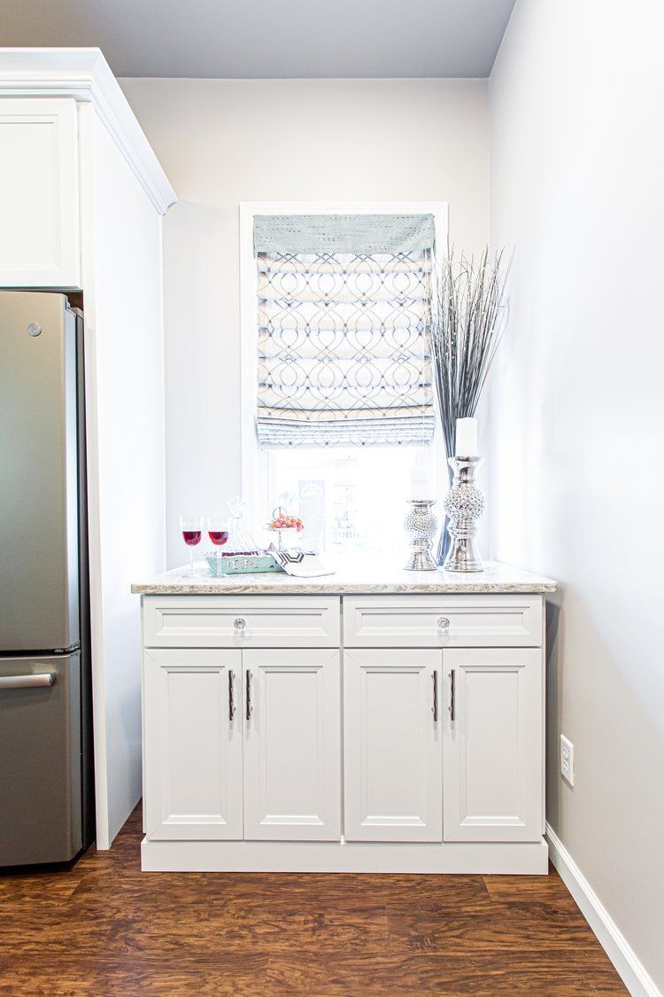 White cabinet with granite countertop, small window with patterned shade, and decorative items.