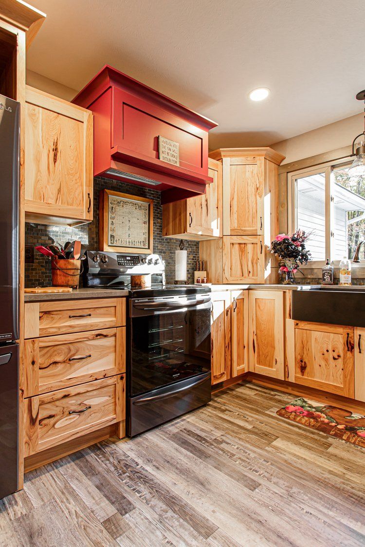 Kitchen with light wood cabinets, red range hood, black stove, and a window.
