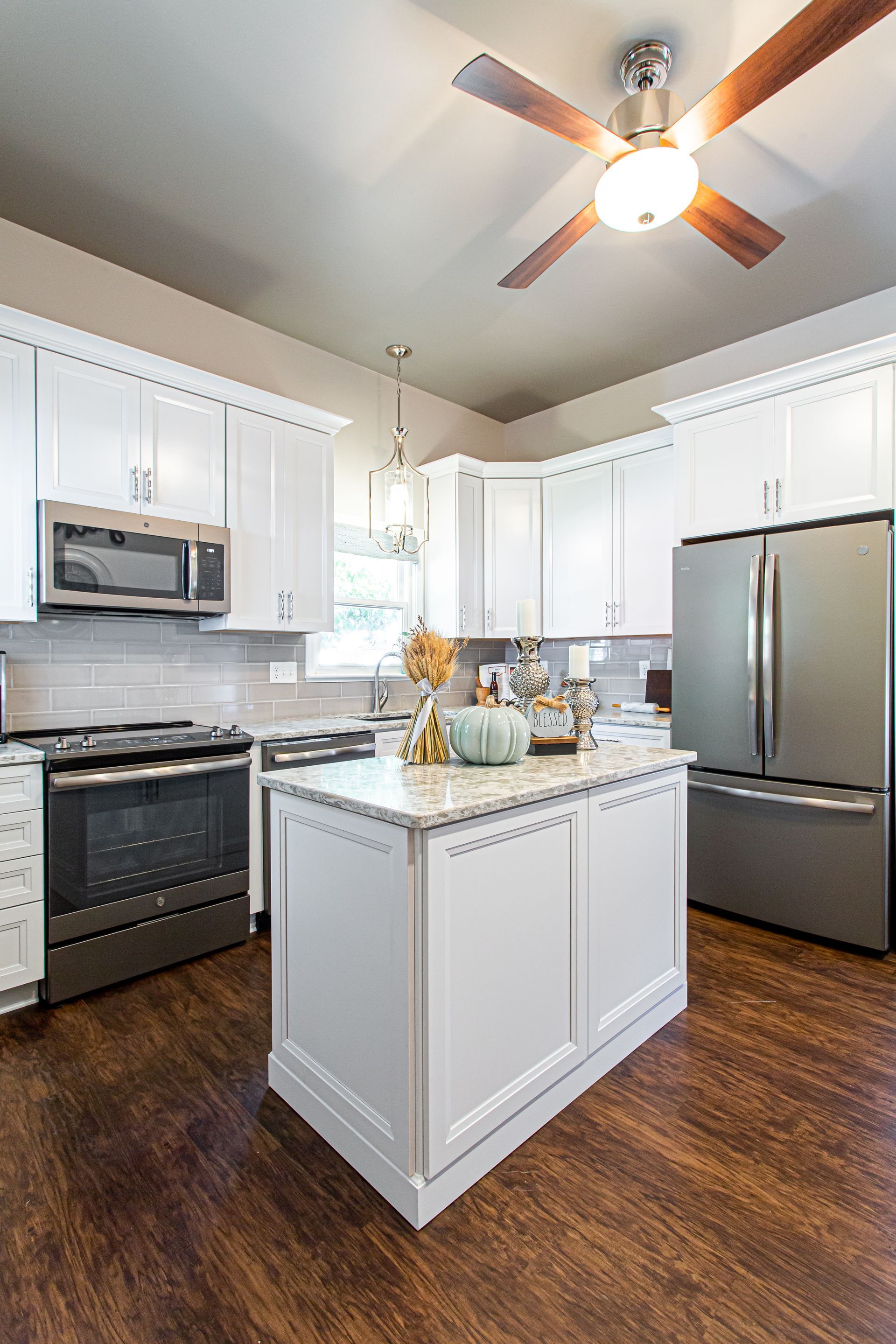 White kitchen with island, stainless steel appliances, and brown wood floors.