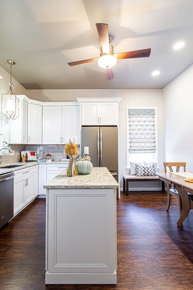 Kitchen with white cabinets, island, and dining area, hardwood floors, and a ceiling fan.