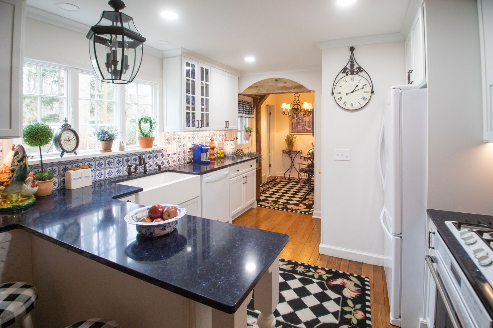 Kitchen with white cabinets, dark countertop, and checkered flooring, leading to a hallway.