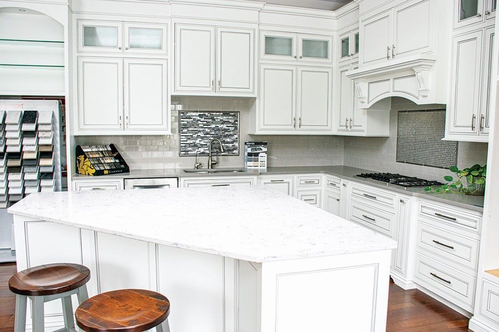 White kitchen with an island, cabinets, countertops, and two stools.
