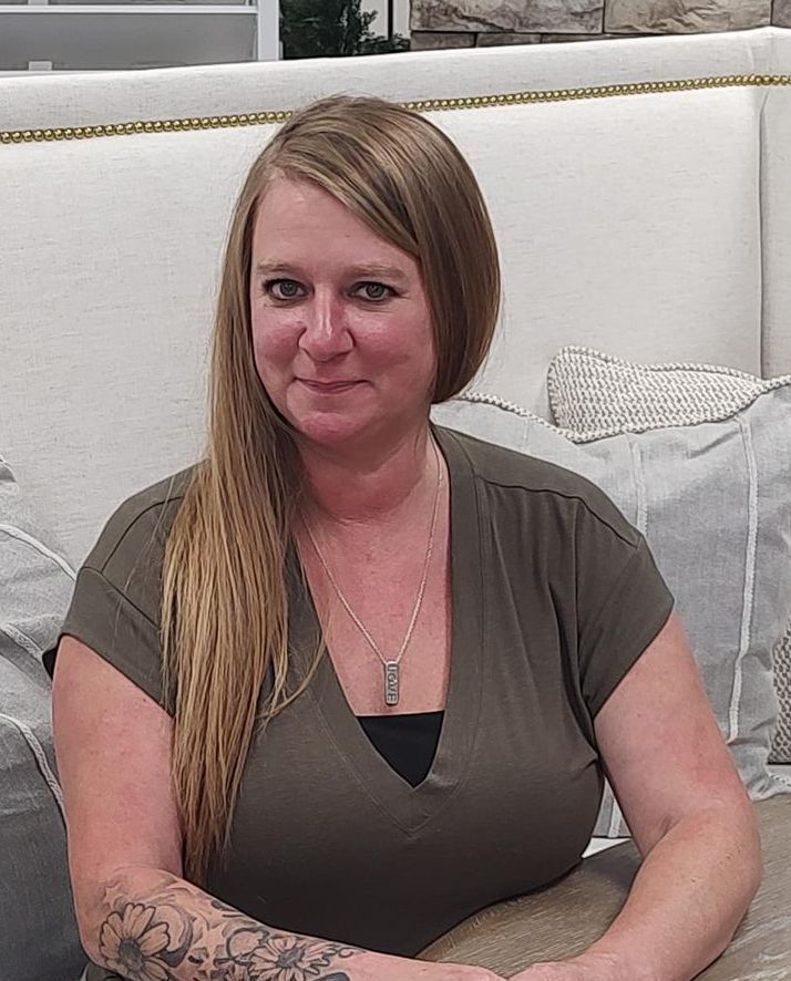 Woman with long blonde hair, wearing a green shirt, sitting with arms crossed, looking at the camera.