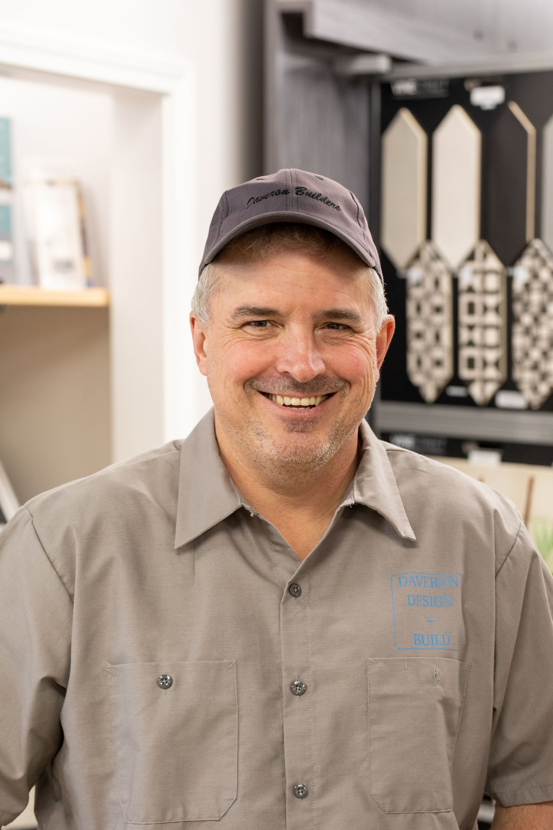 Man in gray work shirt and cap smiles in a tile showroom.