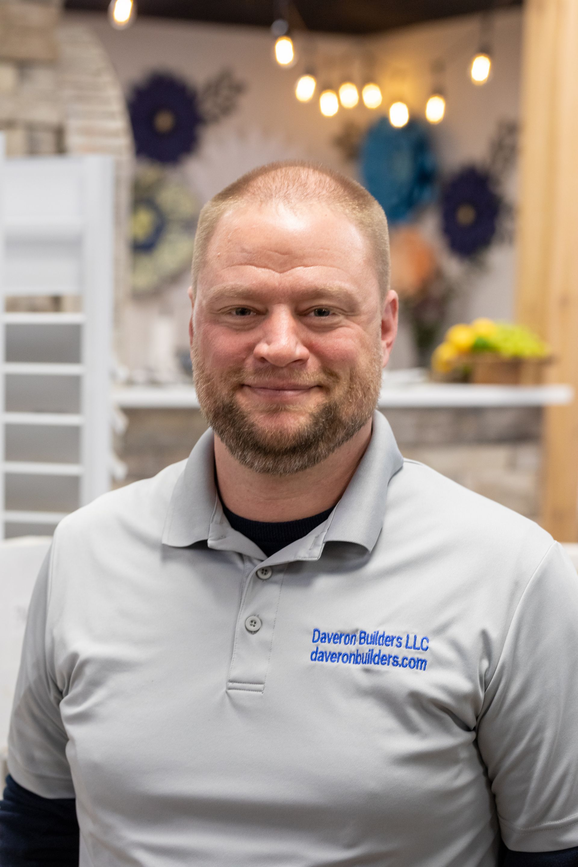 Man wearing a gray polo shirt, smiling, in a showroom-like setting.