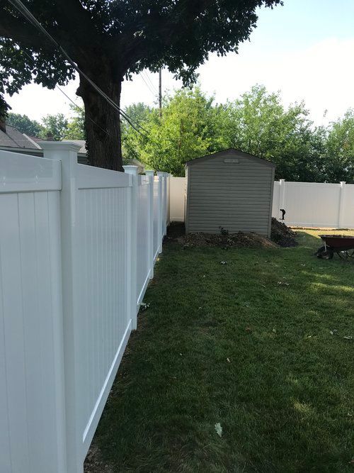 White vinyl fence in a backyard, with a tree, shed, and green grass.