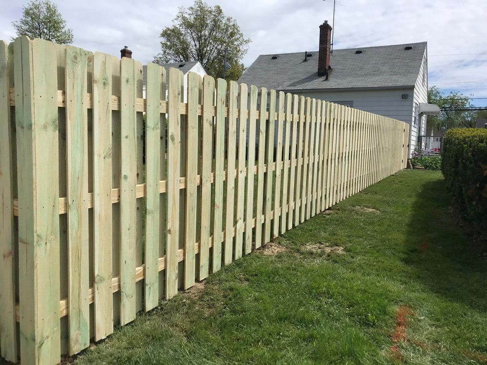 Wooden picket fence in a grassy yard, with a house visible in the background.