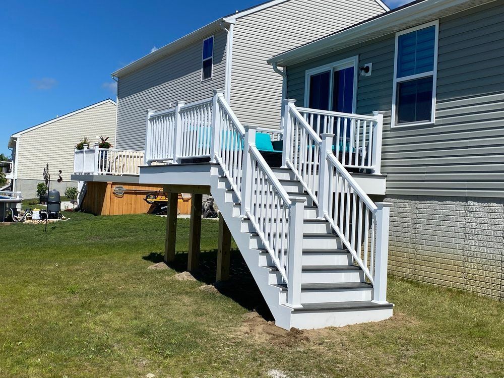 White deck with stairs in a backyard, leading up to a house with blue-tinted windows. Green grass surrounds.