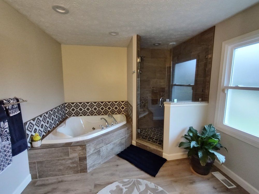 Bathroom with a corner jacuzzi, tiled shower, and a large window.