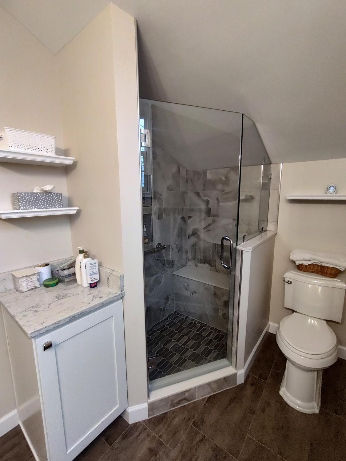 Bathroom with a glass-enclosed shower, toilet, and vanity with shelving.