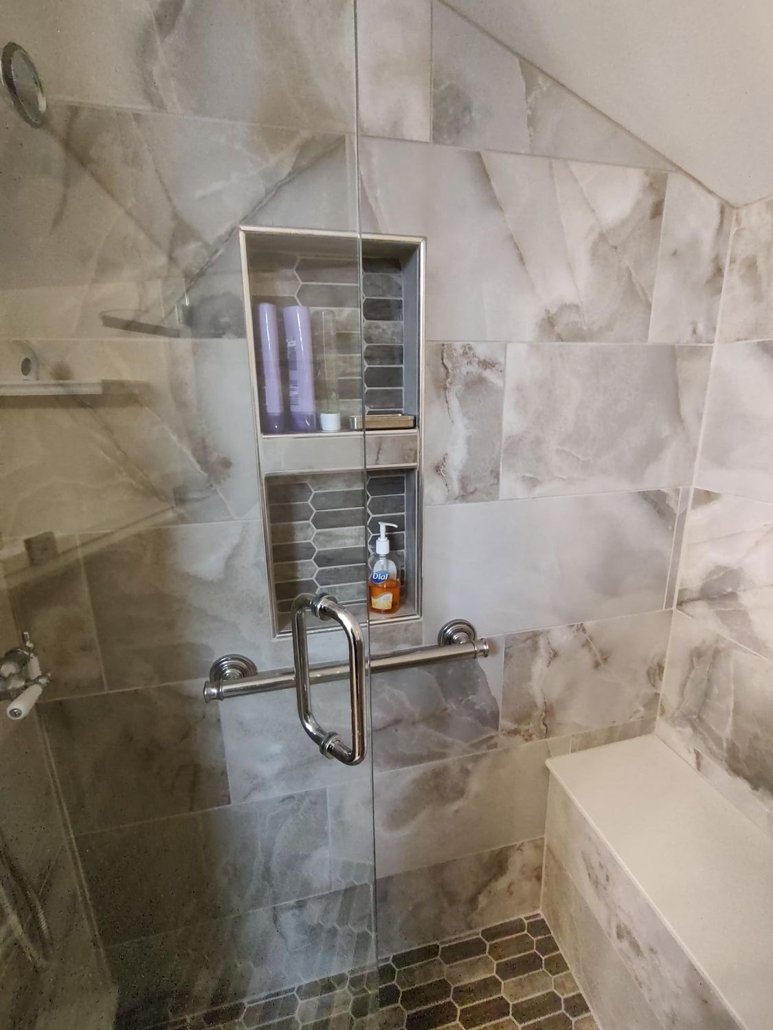 Shower with gray marble tile, glass door, and built-in niche for toiletries; includes a grab bar and bench.
