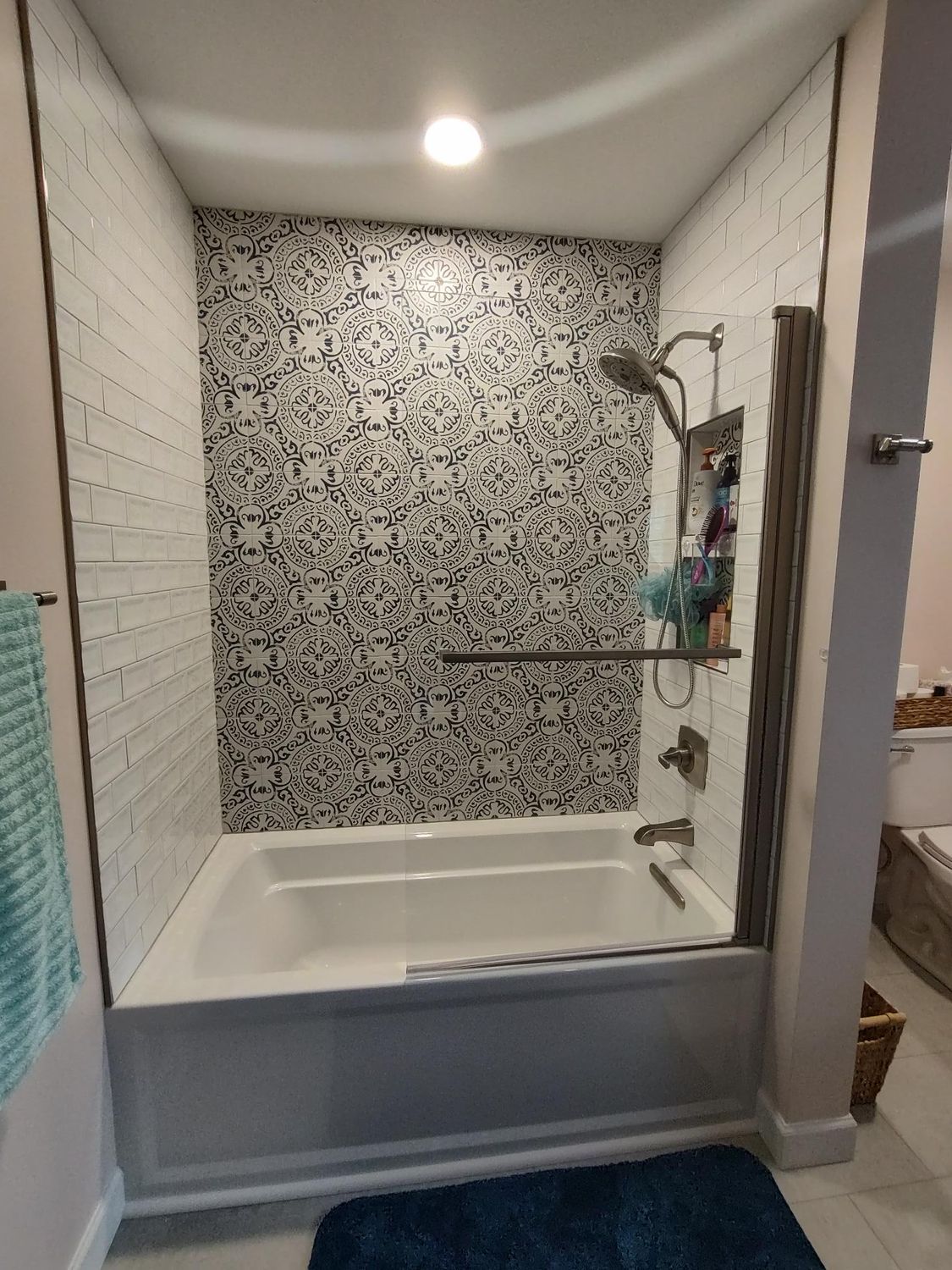 Bathroom with white tub, black and white mosaic tile backsplash, and clear shower glass.