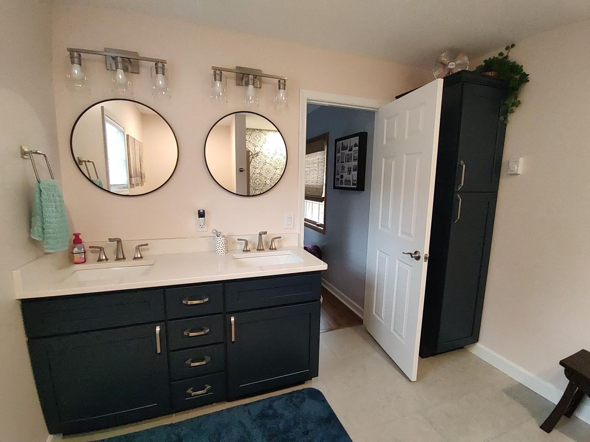 Bathroom with dark blue vanity, round mirrors, and ajar white door.