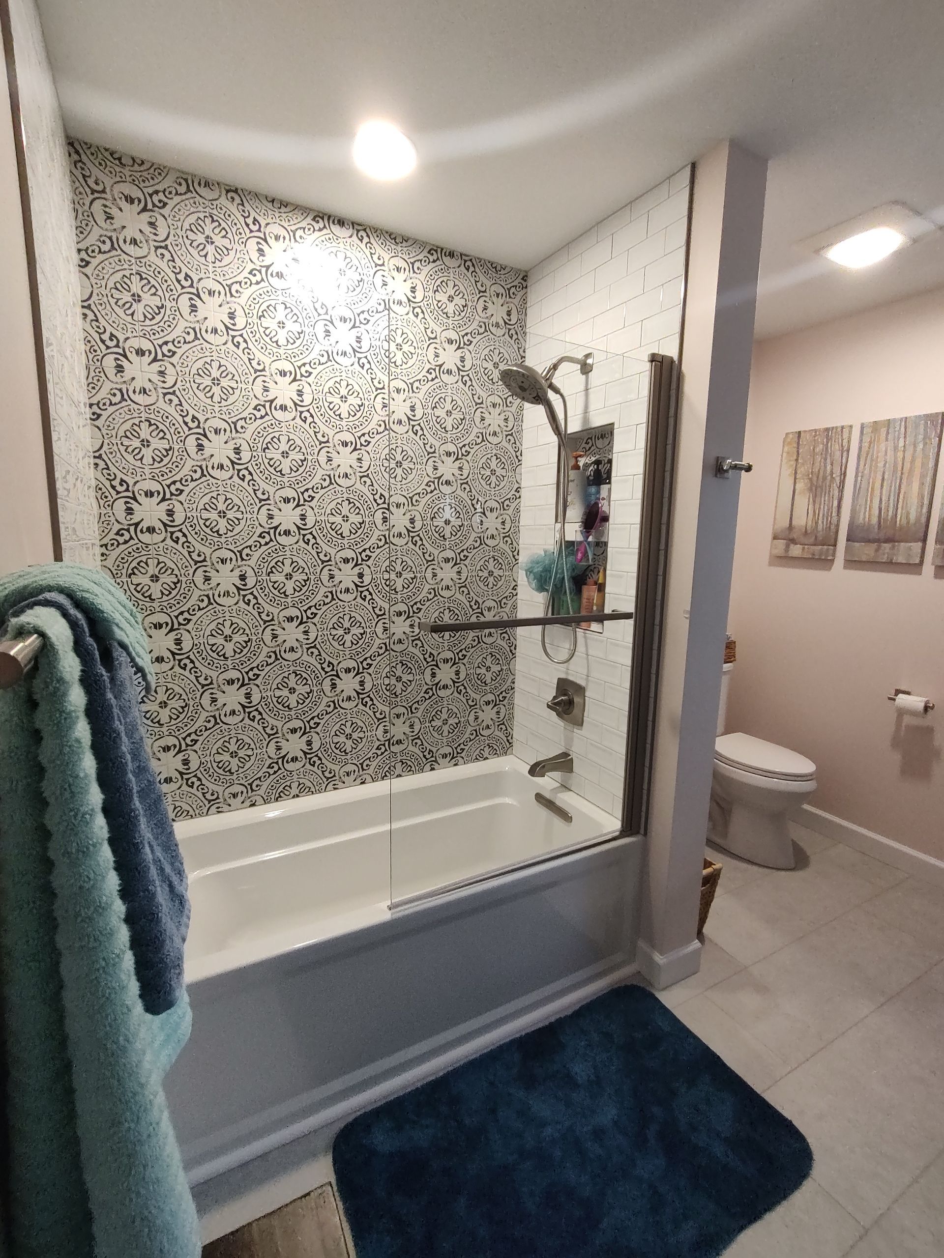 Bathroom with mosaic tile wall, tub, glass shower door, and toilet.