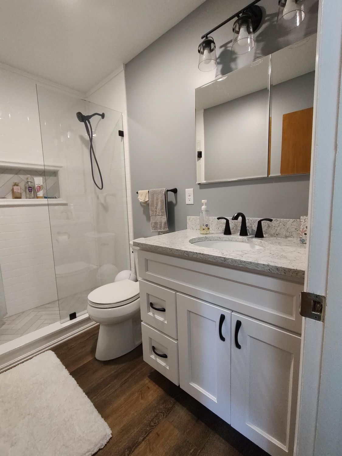 Modern white bathroom with gray walls, a glass shower, and white vanity with a black faucet.
