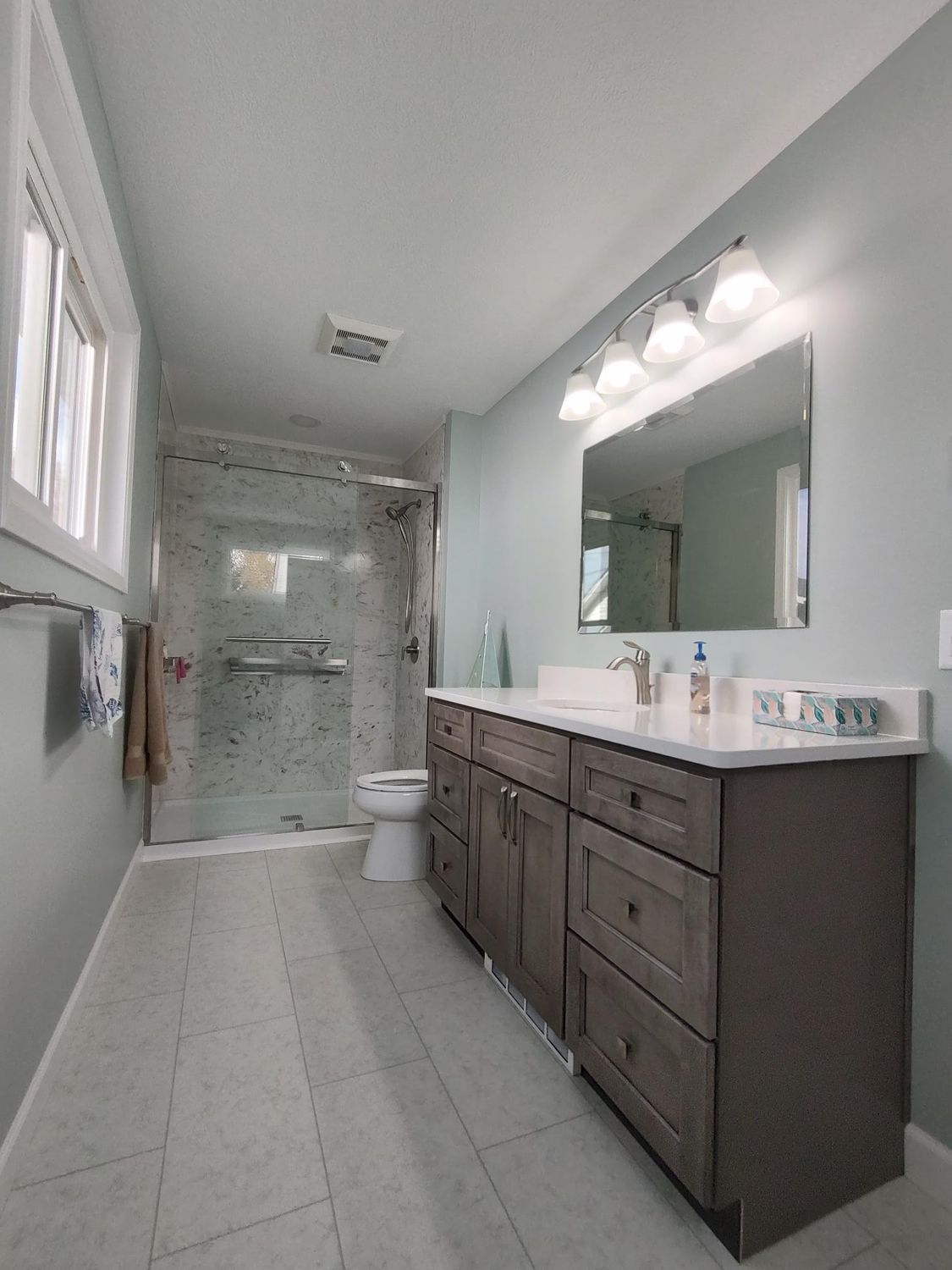 Bathroom with gray vanity, white countertop, large mirror, and glass shower enclosure. Light blue walls and white tile floor.
