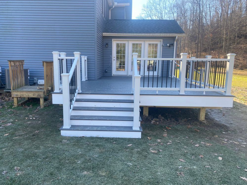 Deck with white railing and black spindles, attached to a gray house, with steps leading to a yard.