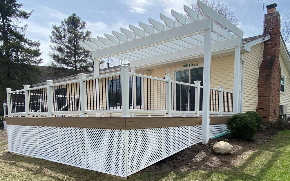White pergola and deck attached to a yellow house with a brick chimney.