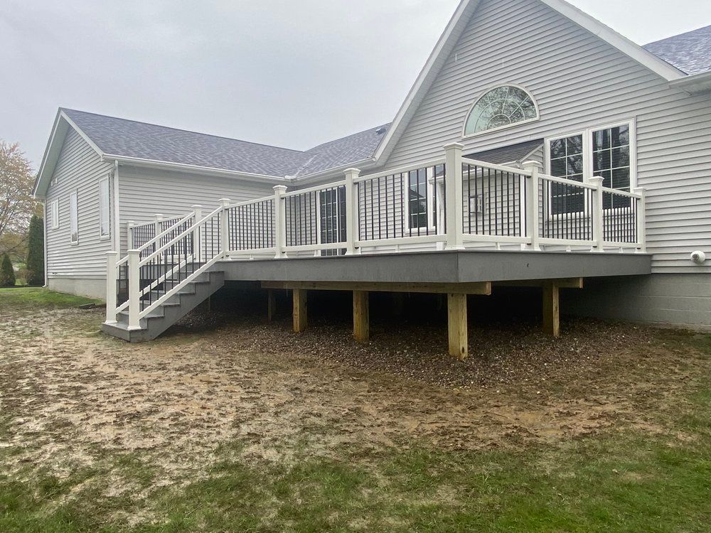 A house with a newly constructed deck. White railing, black accents, and wooden supports.