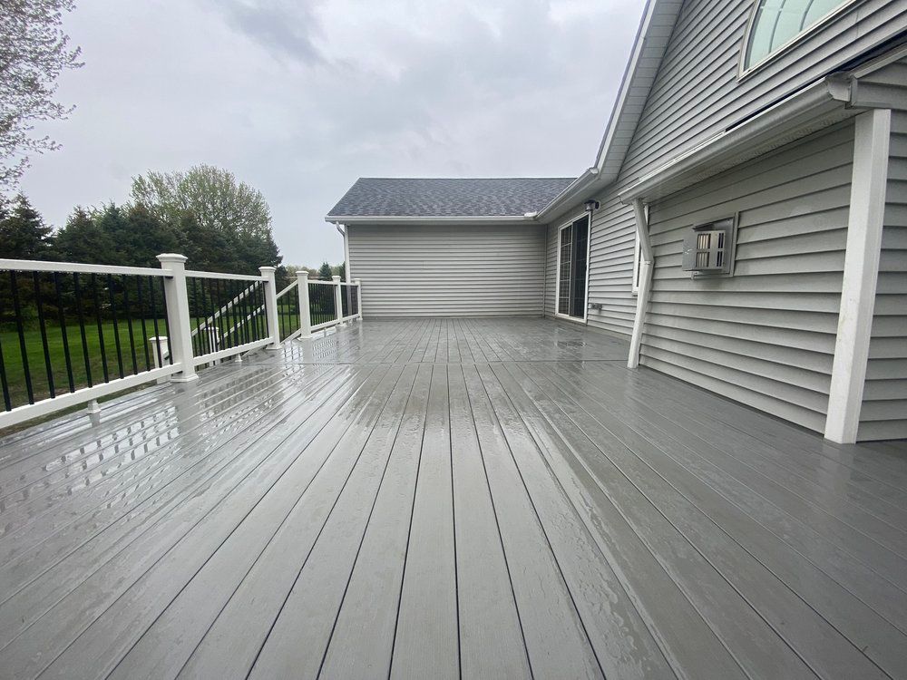 Grey wooden deck outside a grey-sided house with a black railing, under an overcast sky.