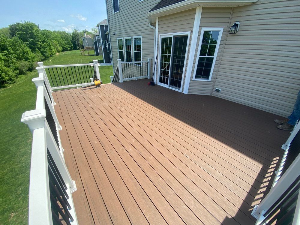 A composite deck with a white railing attached to a light-colored house with a sliding glass door.