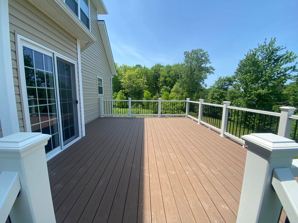 Wooden deck attached to a house with a sliding glass door, overlooking trees under a bright blue sky.