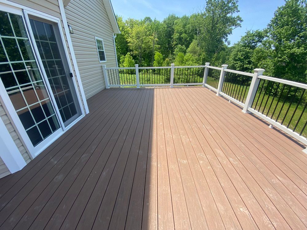 A brown composite deck with white railing overlooks a wooded area. A sliding glass door is on the left.