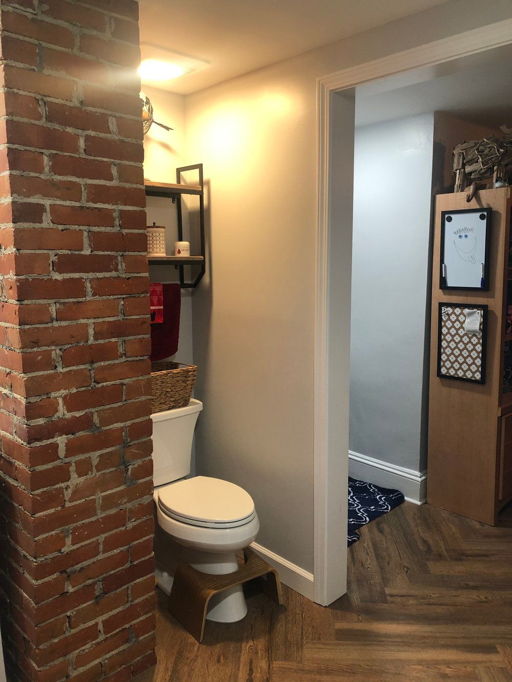 Bathroom with exposed brick, toilet, and wooden flooring. Doorway leads to another room.