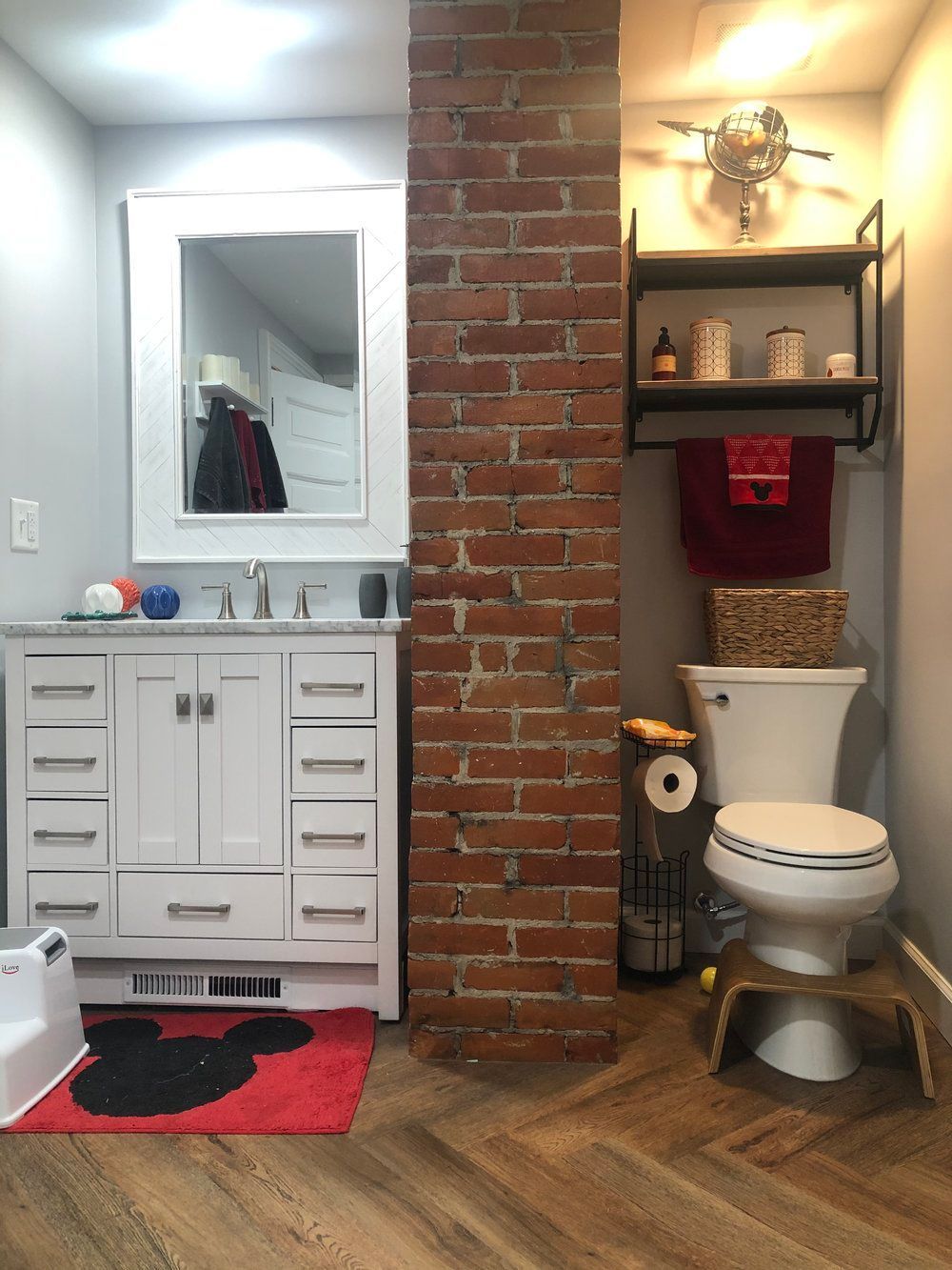 Bathroom with a white vanity, exposed brick column, and a toilet with a step stool.