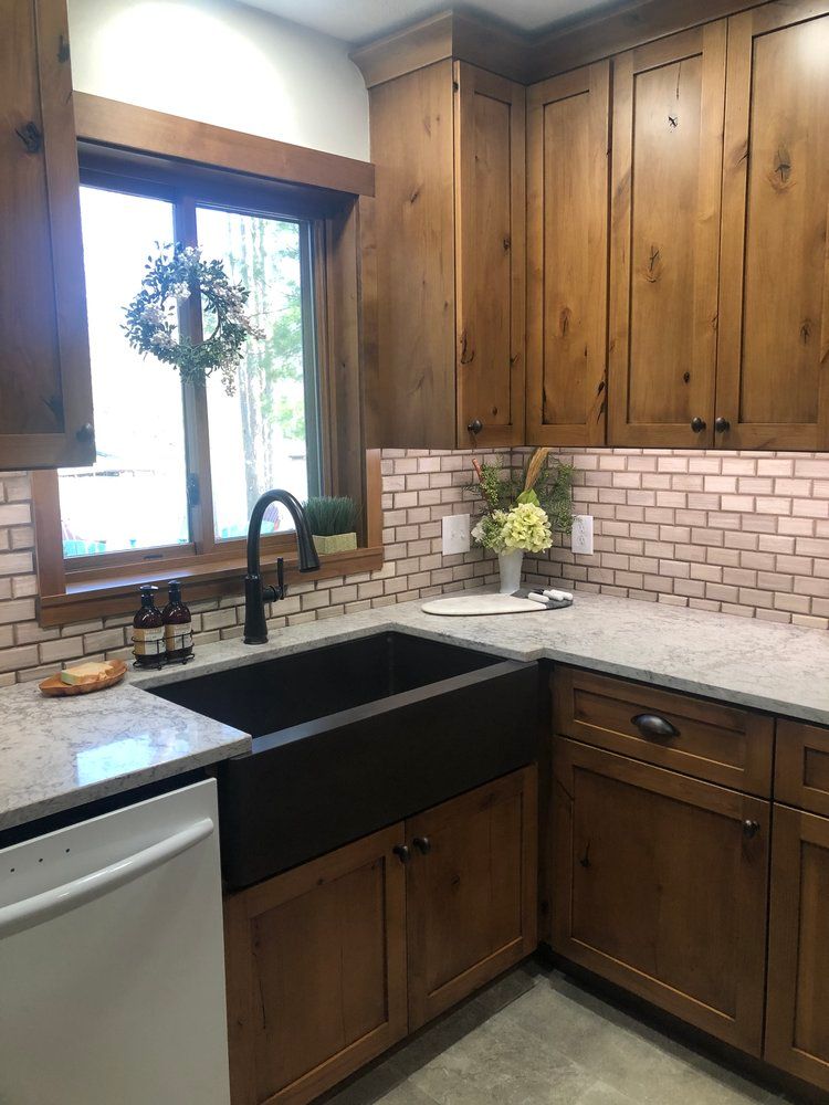 Rustic kitchen with wooden cabinets, black sink, and light pink tile backsplash.