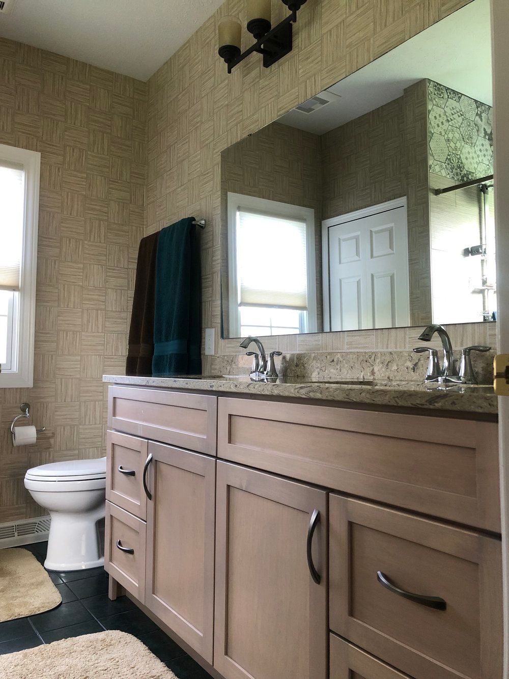 Bathroom with a double sink vanity, toilet, and textured wallpaper.