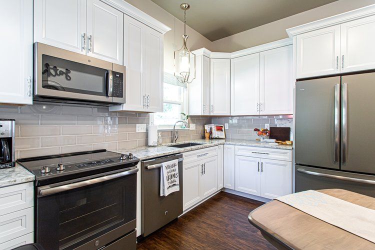 White kitchen with stainless steel appliances, white cabinets, and dark wood floors.