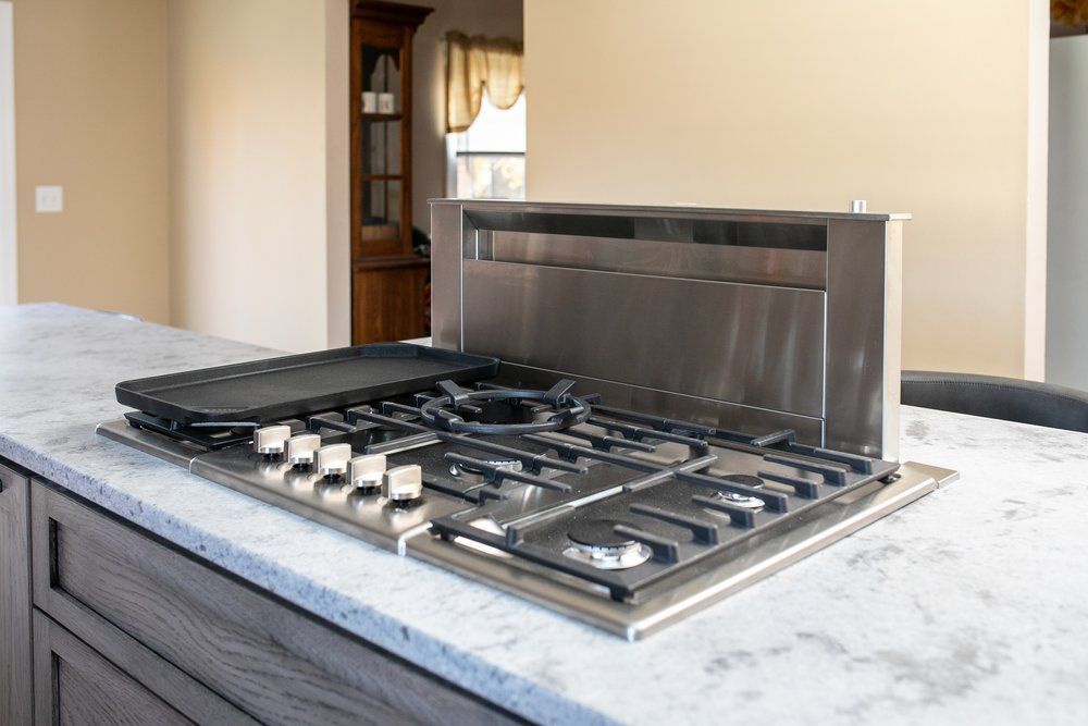 Stainless steel gas cooktop with griddle on a kitchen island, with a pop-up vent.