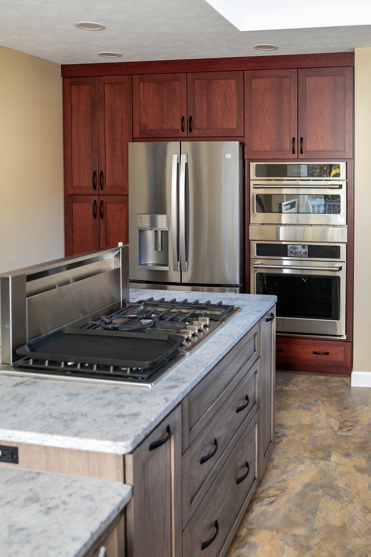 Modern kitchen with dark wood cabinets, stainless steel appliances, and a gray island with a cooktop.