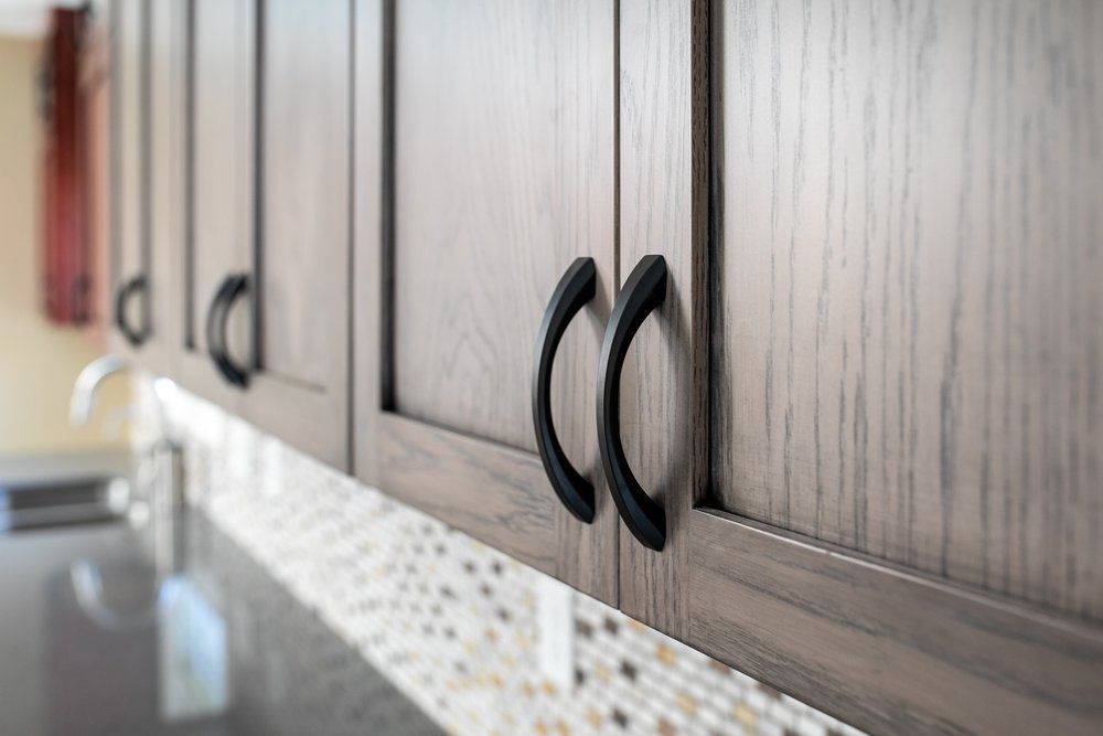 Close-up of kitchen cabinets with dark handles, above a tiled backsplash and countertop.