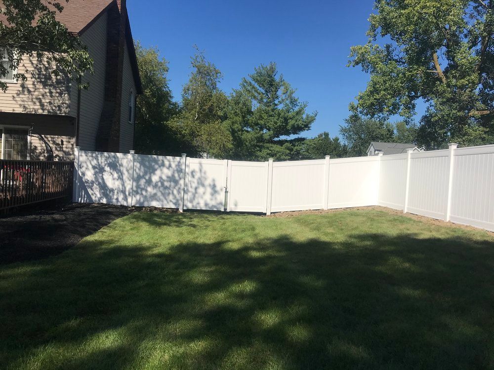 White vinyl fence in a backyard, with green grass and trees under a blue sky.