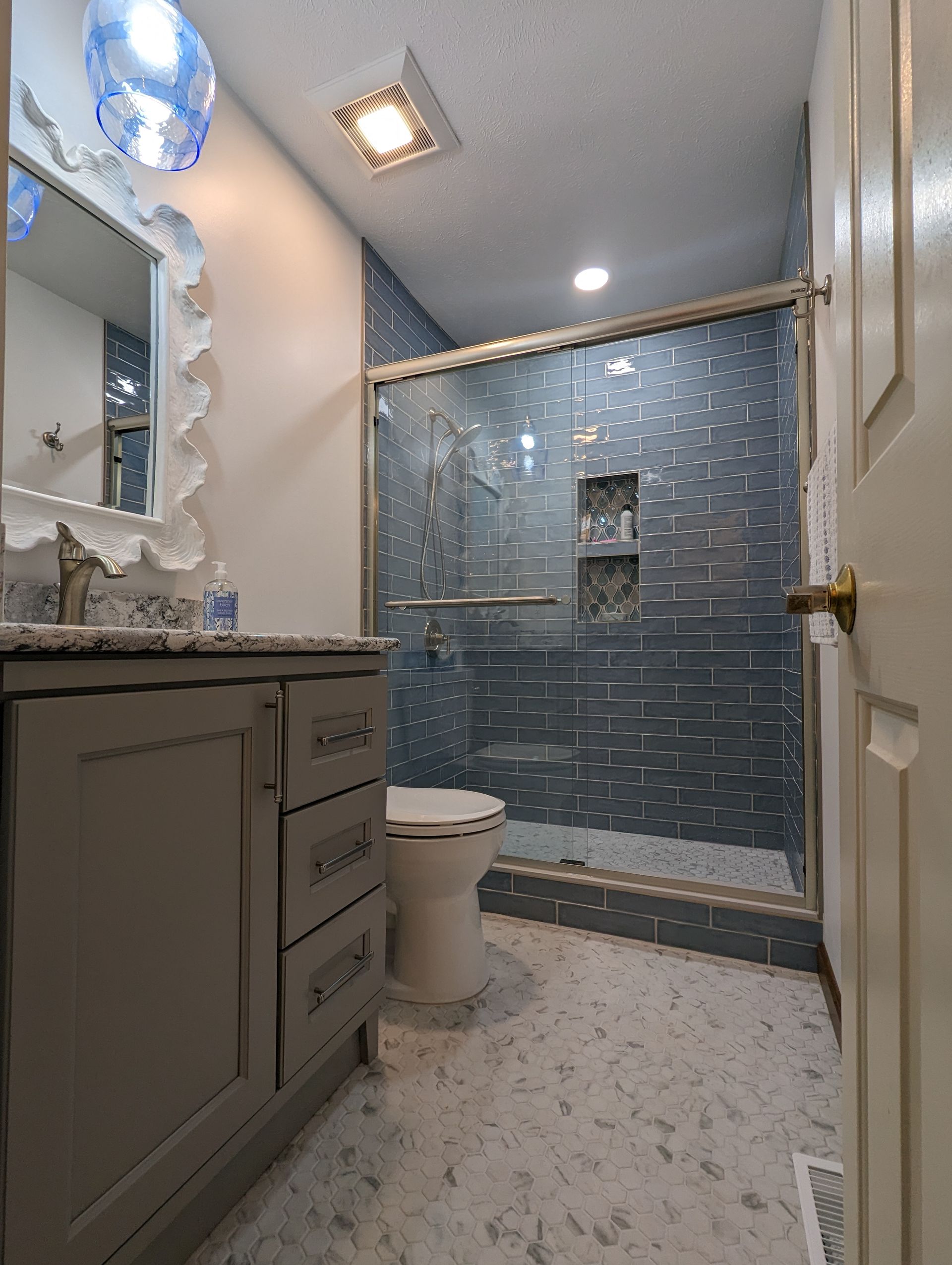 Bathroom with gray vanity, patterned tile, blue tiled shower, and a white toilet.