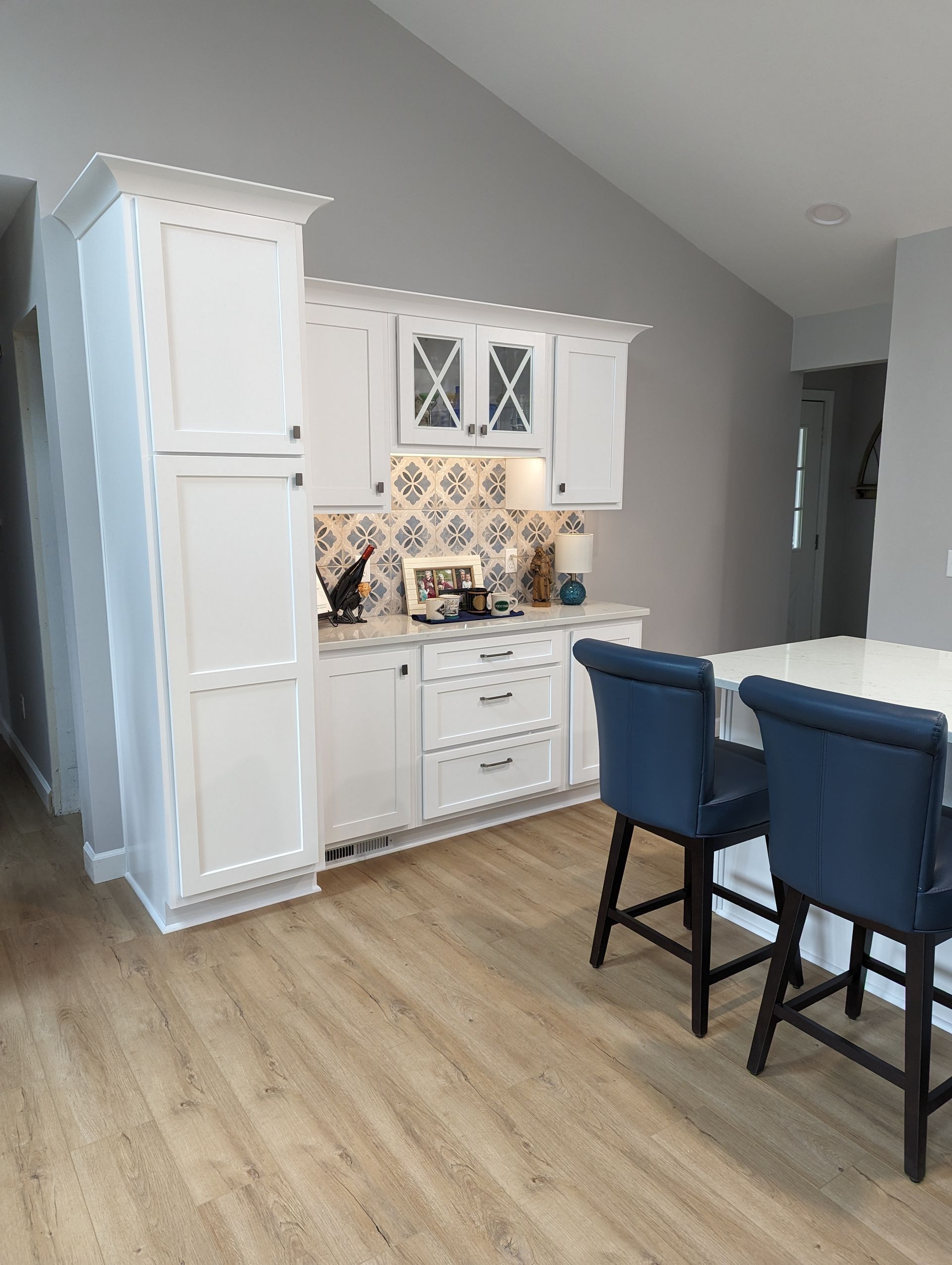 White kitchen cabinets with blue chairs, tile backsplash, and light wood flooring.