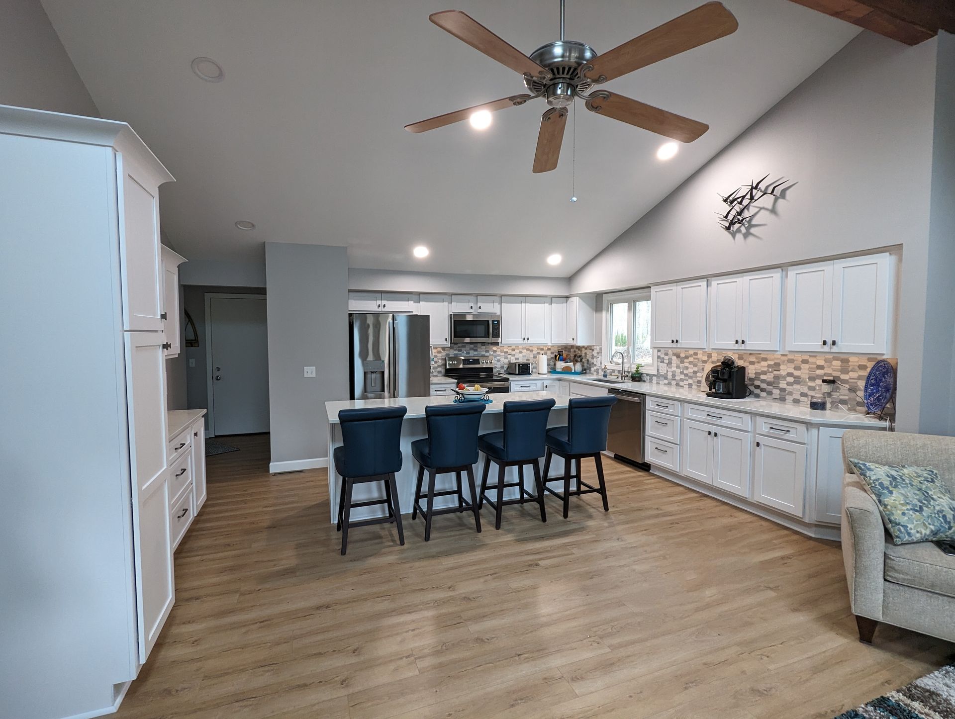 Bright kitchen with white cabinets, island with blue stools, stainless steel appliances, and wooden floors.