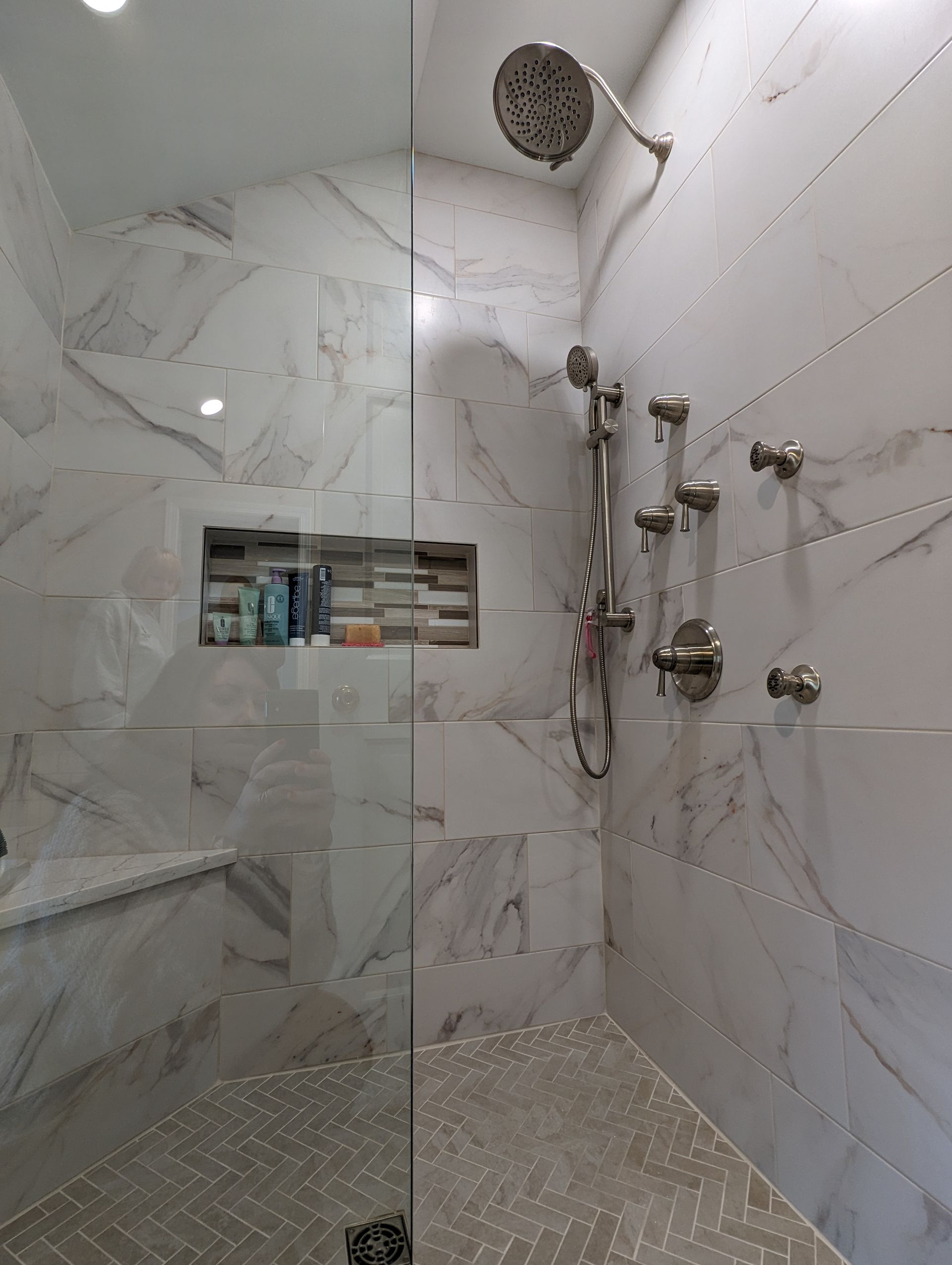 Modern shower with marble-like tile, built-in shelf, glass door, and silver shower fixtures.