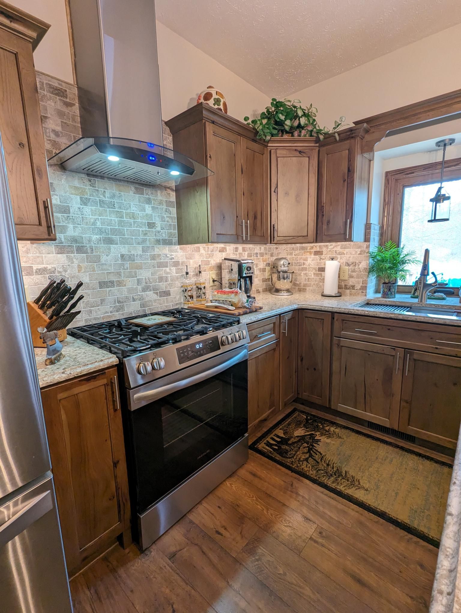 Kitchen with stainless steel range, wooden cabinets, patterned backsplash, and area rug on wood floor.