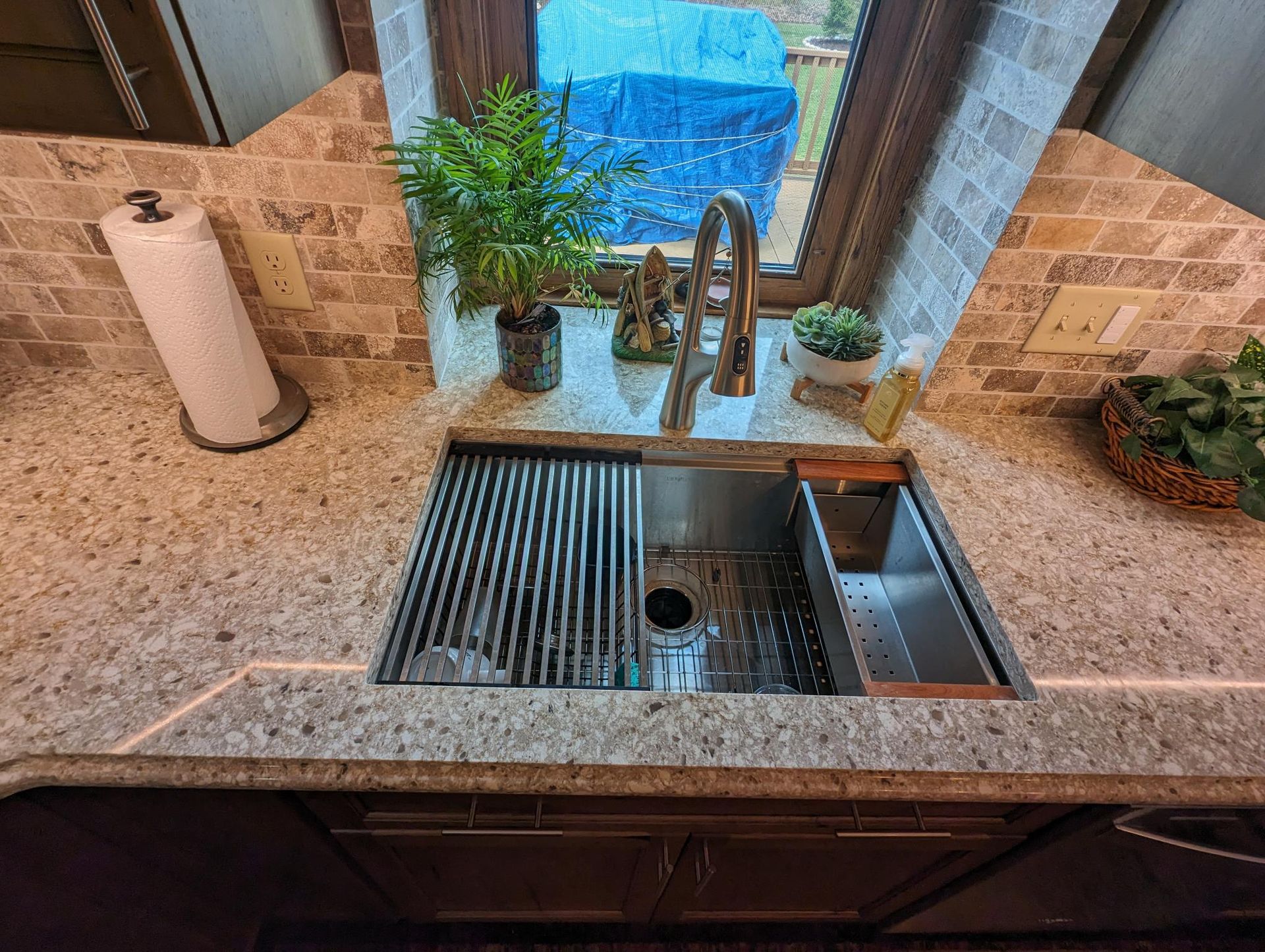 Kitchen sink with stainless steel basin and accessories, granite countertop, neutral colors.